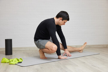 Young man doing a hamstring stretch on a yoga mat at home, practicing fitness