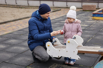 Father playing with toddler daughter on a seesaw at an outdoor playground in winter