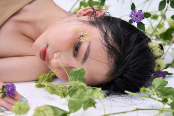 Young woman posing with a gentle expression, adorned with floral elements on her body."
