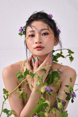 Young woman posing elegantly with arms raised, surrounded by climbing plants and blossoms."