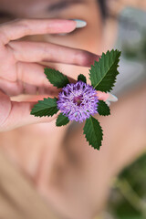 lose-up of a young woman's hand holding a small purple flower against a neutral background.