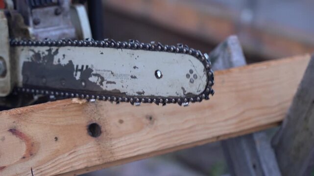 Close-Up of Chainsaw Bar and Chain Positioned Near Wooden Plank, Showcasing the Tool's Functionality and Detail in Woodworking or Tree Maintenance Context. Video with sound