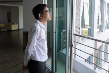 Asian businessman thinking, planning, finding a good solution or idea, looking outside through office building window