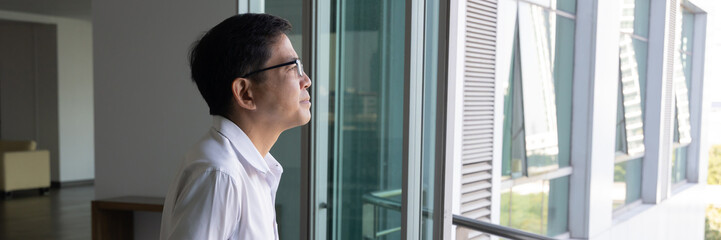 Asian businessman thinking, planning, finding a good solution or idea, looking outside through office building window