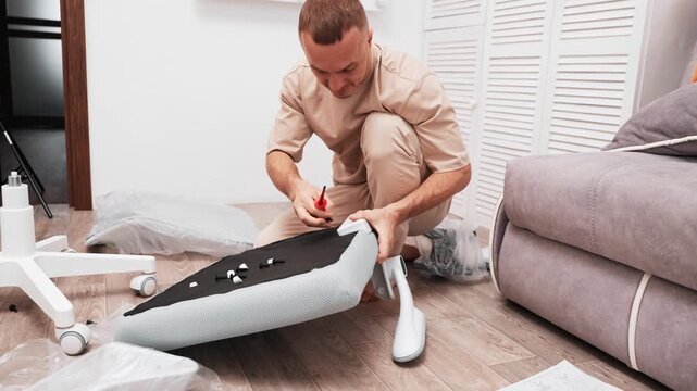 Man carefully assembles chair, tightening screws and adjusting parts on floor. Scene captures focused moment of practical home work, surrounded by tools, details, and step-by-step effort.