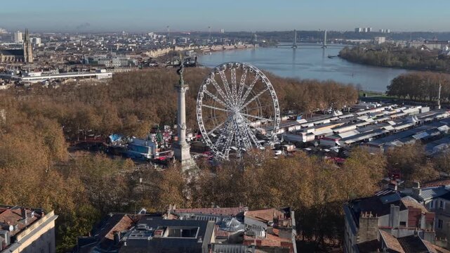 Aerial view of Bordeaux Quinconces, bustling riverside fair with a giant Ferris wheel in a vibrant city landscape