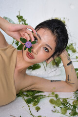 The woman reclining with arms raised, adorned with floral elements and green foliage.