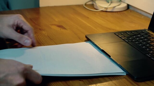 Close-up hands pushing laptop aside and pulling spiral notebook closer reorganizing workspace switching from digital to analog notes home office creative work evening warm light