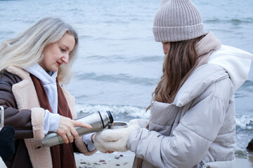 Family drinking hot tea and spending time outdoors  on a cold seaside beach, . Winter lifestyle scenes with warm clothing, coastal environment and everyday activities.