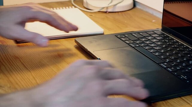 Close-up hands pushing laptop aside and pulling spiral notebook closer reorganizing workspace switching from digital to analog notes home office creative work evening warm light