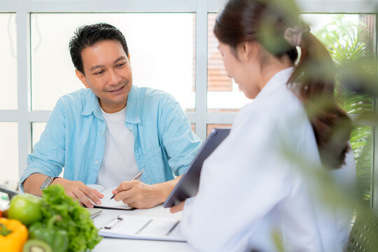 Asian nutritionist using tablet to explaining personalized meal plan with AI to patient during healthcare consultation, healthy lifestyle, woman dietitian showing nutrition plan with AI on tablet.
