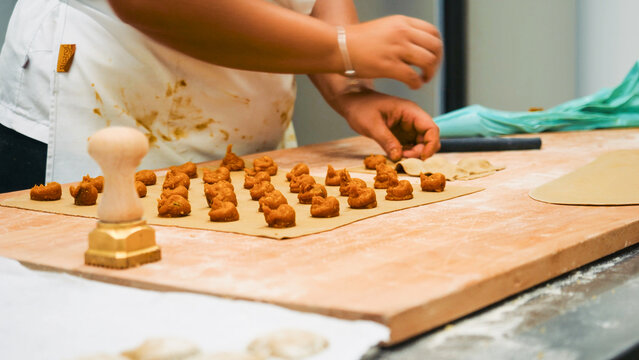 Artisan hands preparing fresh pasta on a wooden board at a traditional Italian kitchen, making homemade ravioli with filling and a pasta stamp - Powered by Adobe