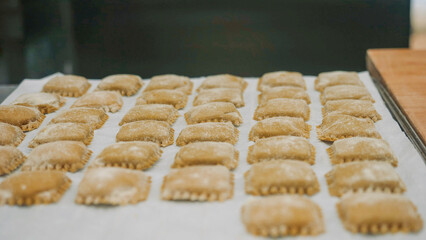 Hands placing rows of freshly made square pasta, traditional Italian ravioli prepared on a baking sheet, ready for cooking in a kitchen environment