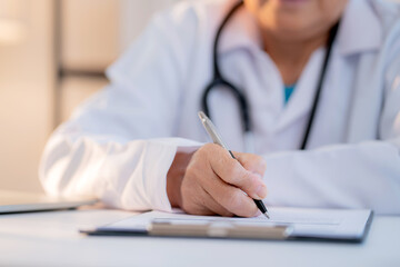 Close up senior asian doctor writing prescription or document on clipboard in clinic office, managing patient record, healthcare and diagnosis, elderly female physician writing on paperwork.