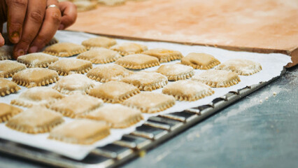 Hands placing rows of freshly made square pasta, traditional Italian ravioli prepared on a baking sheet, ready for cooking in a kitchen environment