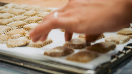 Hands shaping fresh ravioli on a floured wooden board, using a manual cutter to craft rustic, handmade pasta pieces for an authentic Italian kitchen experience