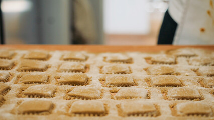 Human hands gently moving and dusting rows of freshly made, uncooked pasta, highlighting the careful, artisanal process of creating traditional culinary dishes by hand