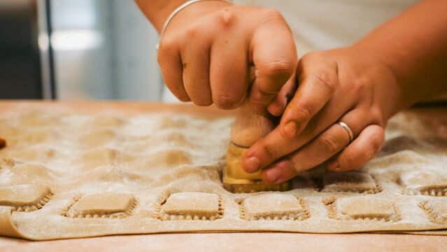 Human hands gently moving and dusting rows of freshly made, uncooked pasta, highlighting the careful, artisanal process of creating traditional culinary dishes by hand