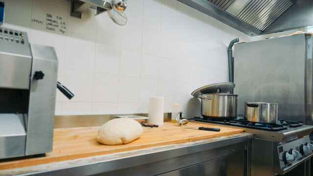 Fresh dough resting on a wooden board in a professional stainless steel kitchen, preparing ingredients for baking bread, pizza, or pastries in a restaurant setting - Powered by Adobe