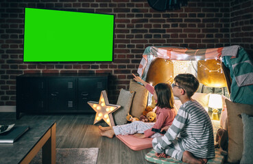 Two children in pajama sitting while watching television film on living room. Domestic life concept.