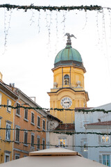 Naklejka premium The iconic City Clock Tower (Gradski Toranj) in Rijeka, Croatia, framed by festive Christmas lights hanging across the street