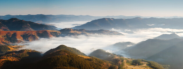 Atmospheric top view of the valley of the village Dzembronya shrouded in soft white fog during early morning. Carpathian mountains, Ukraine, Europe.