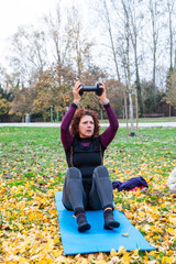 Woman exercising outdoors doing sit-ups with dumbbell