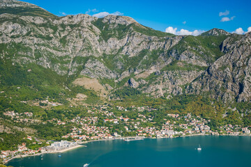 Naklejka premium Aerial view of a coastal town Risan in Montenegro, surrounded by mountains and clear blue water. Lush greenery and small boats are visible in the bay.
