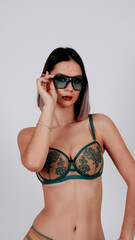 Woman in green lingerie and sunglasses raising her hand toward the camera