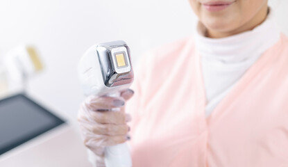 Female technician using laser device for hair removal treatment, studio white light