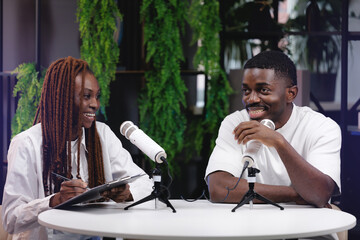 Two African American podcasters engaging in lively discussions with microphone hosting podcast in...