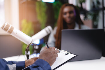 African adult podcasting session with speaker and microphones and laptop in studio