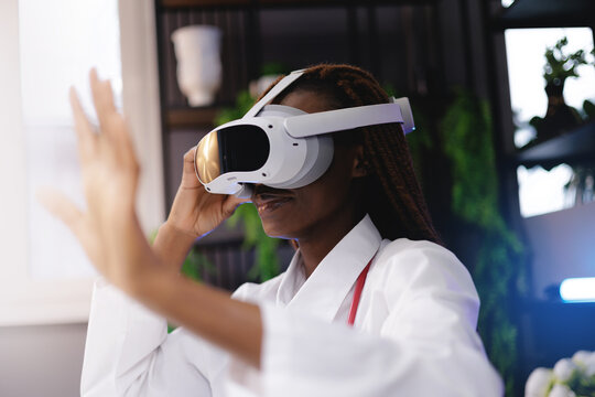 Portrait happy African female doctor using virtual reality headset in medical innovation concept, gesture with finger to press button, sunlight