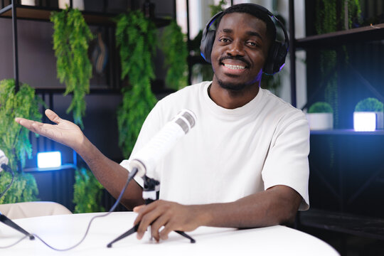 Portrait happy African male podcast host in studio with headphones and microphone in broadcast studio or recording video for blog