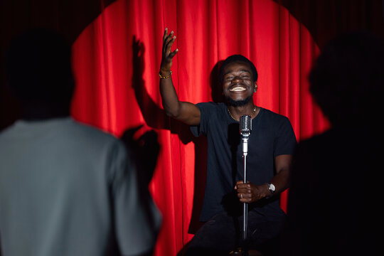 Happy young african american man comic tells stand up monologue on stage with red curtains. Concept humor standup comedian show open mike
