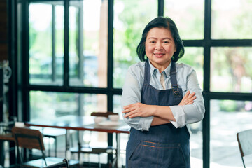 Asian senior female restaurant owner wearing apron standing confidently smiling proudly in cafe representing leadership teamwork and successful small business management lifestyle