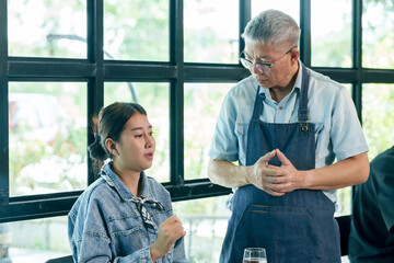 Asian elderly restaurant owner standing beside female customer discussing feedback about meal, warm respectful conversation, teamwork hospitality concept, small business cooperation, lifestyle showing