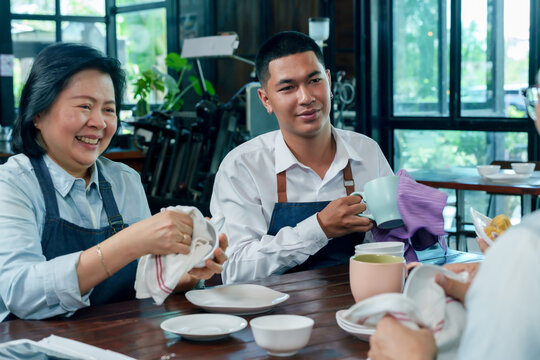 Asian senior female owner and young barista smiling together while cleaning dishes teamwork concept cafe restaurant small business cooperation family hospitality management communication friendly