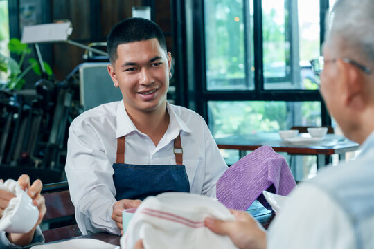 Asian young male barista wearing apron talking with senior owner while cleaning dishes teamwork cafe restaurant small business cooperation family communication hospitality management friendly service