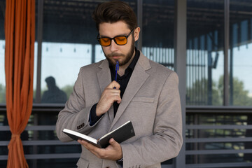 Man in suit and sunglasses holding a book,standing in front of a office building