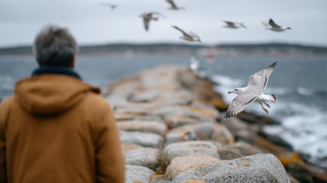 A contemplative man gazing at seagulls flying over the shoreline, capturing a moment of introspection and connection with nature at a rocky ocean landscape. - Powered by Adobe