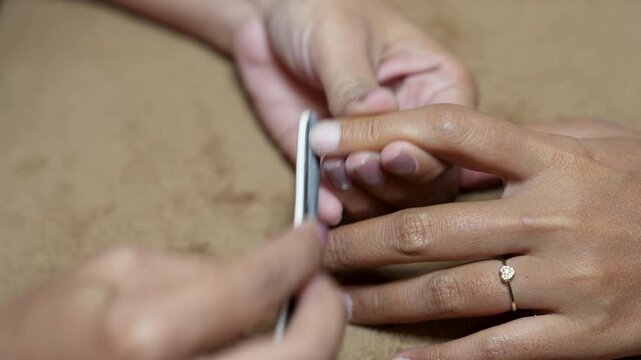 Close up of manicurist using nail file and buffer to shape and smooth fingernail in beauty salon for nail care concept.