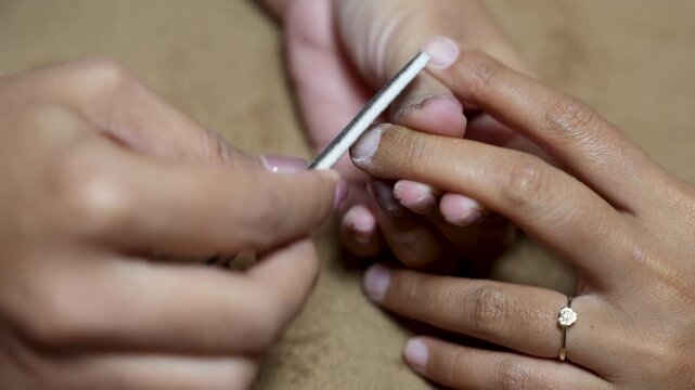 Close up of manicurist using nail file and buffer to shape and smooth fingernail in beauty salon for nail care concept.