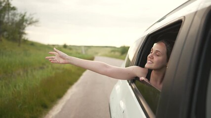 Stretching hand from car window as woman smile while driving along countryside road with green grass and rolling hill travel mood summer carefree vibe wind in hair close view of hand and window