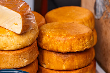 Cheese wheels of aged cheese lie at the farmers' market. Cheese wheels made on a dairy farm. Dairy products. Smoked cheese.
