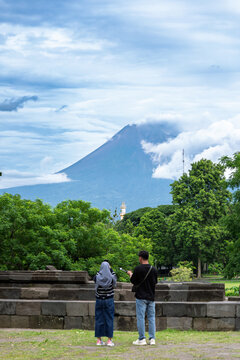 Java Indonesia 12 11 2025 &ndash; Two local tourists taking photos from behind with Mount Merapi rising in the background on a clear day.