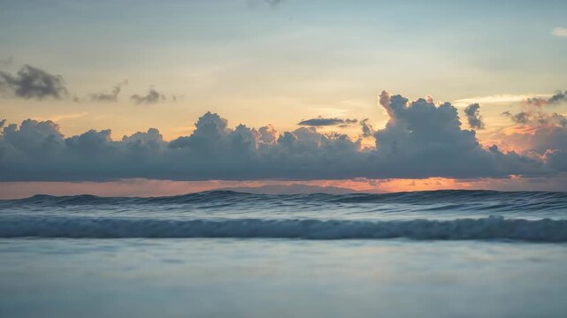 Wide view of ocean waves gently rolling towards shore at sunset with soft light illuminating colorful clouds and tranquil water surface creating a serene natural landscape
