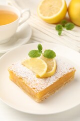 Tasty lemon bar with powdered sugar and mint served on white wooden table, closeup