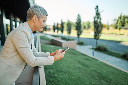 Portrait of a young businesswoman woman using a smartphone mobile phone walking down the street, surrounded by moder corporate office buildings