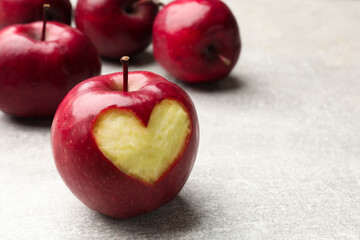 Ripe apple with carved heart and whole ones on grey textured table, closeup. Space for text